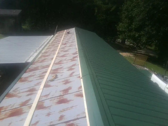 Old rusted panels beside newly installed green metal roofing — Wind Damage Roof Repair by Roofing Brothers in Farmington